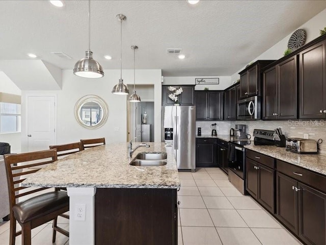 kitchen featuring stainless steel appliances, an island with sink, sink, and a kitchen bar