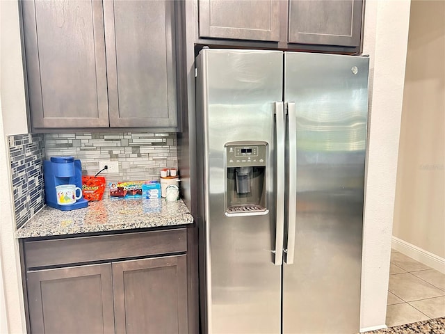 kitchen featuring dark brown cabinetry, light stone countertops, backsplash, stainless steel fridge, and light tile patterned flooring