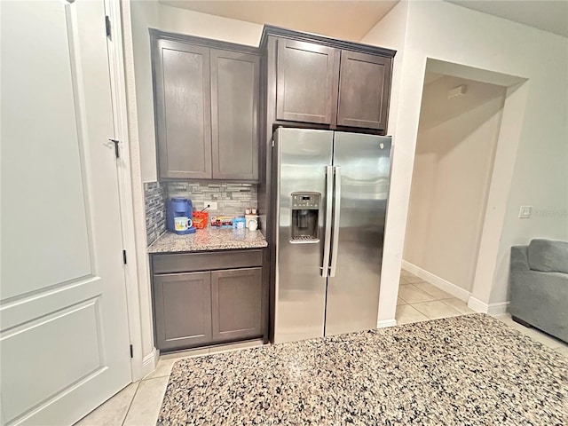 kitchen featuring stainless steel refrigerator with ice dispenser, decorative backsplash, light tile patterned floors, light stone counters, and dark brown cabinetry