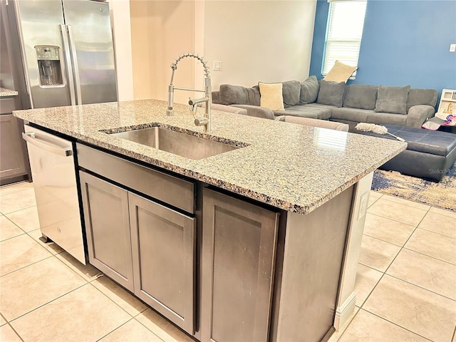 kitchen featuring a center island with sink, light stone counters, sink, and appliances with stainless steel finishes