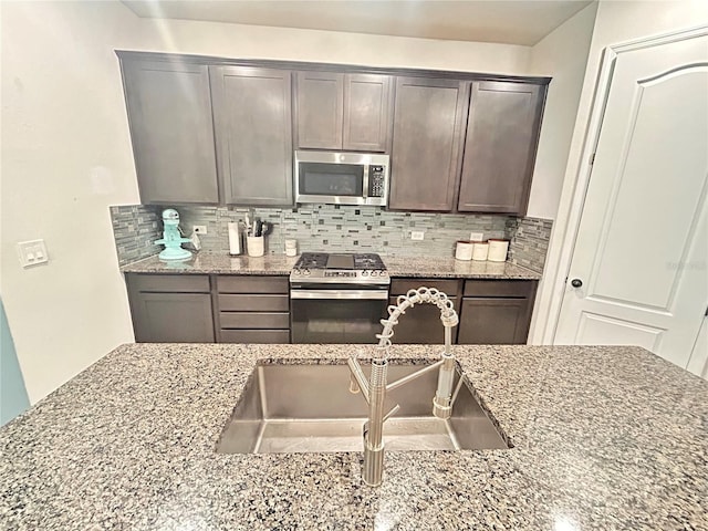 kitchen with sink, light stone countertops, appliances with stainless steel finishes, tasteful backsplash, and dark brown cabinetry