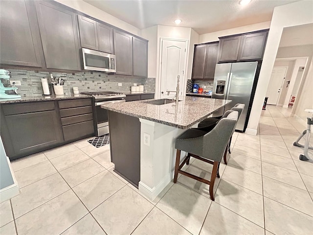 kitchen featuring light stone countertops, stainless steel appliances, sink, a center island with sink, and a breakfast bar area