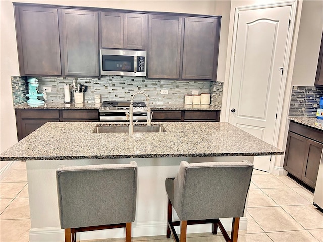 kitchen with light tile patterned flooring, a kitchen bar, light stone countertops, and a kitchen island with sink