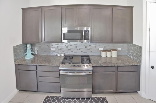 kitchen featuring appliances with stainless steel finishes, decorative backsplash, light tile patterned floors, and stone countertops