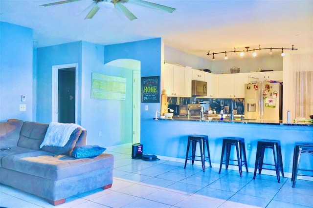 kitchen featuring tile patterned flooring, backsplash, stainless steel fridge with ice dispenser, a peninsula, and white cabinets