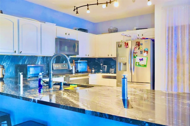 kitchen with appliances with stainless steel finishes, dark stone counters, white cabinets, sink, and backsplash