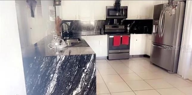 kitchen featuring a sink, tasteful backsplash, white cabinetry, appliances with stainless steel finishes, and light tile patterned floors