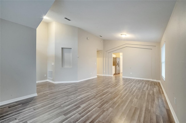 spare room featuring light wood-type flooring and vaulted ceiling