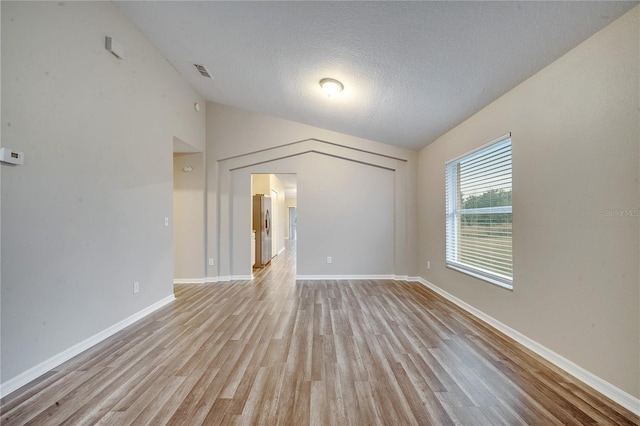 empty room featuring a textured ceiling, light wood-type flooring, and vaulted ceiling