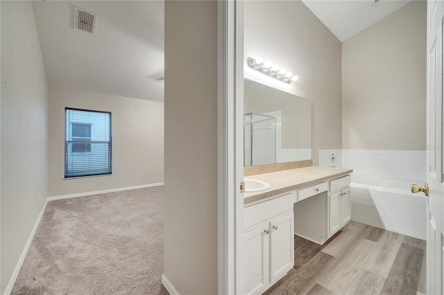 bathroom featuring hardwood / wood-style floors, vanity, a textured ceiling, and a relaxing tiled tub