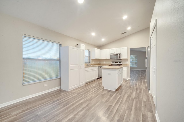 kitchen featuring stainless steel appliances, white cabinets, a center island, lofted ceiling, and light wood-type flooring