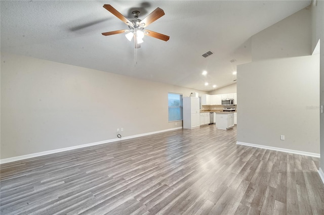 unfurnished living room featuring light wood-type flooring, ceiling fan, vaulted ceiling, and a textured ceiling