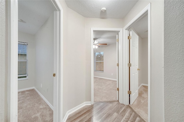 corridor with a textured ceiling and light wood-type flooring