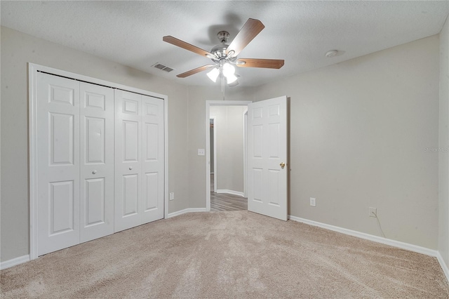 unfurnished bedroom featuring ceiling fan, a closet, light carpet, and a textured ceiling