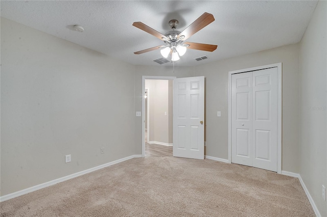 unfurnished bedroom with light carpet, a textured ceiling, a closet, and ceiling fan