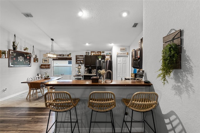 kitchen with dark hardwood / wood-style floors, kitchen peninsula, sink, stainless steel fridge with ice dispenser, and a breakfast bar area