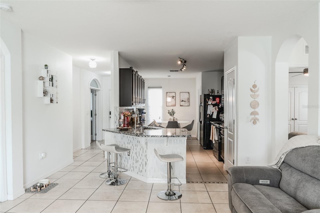 kitchen with light tile patterned flooring, black appliances, sink, a kitchen breakfast bar, and kitchen peninsula