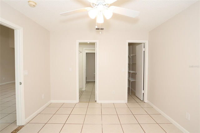 unfurnished bedroom with ceiling fan, light tile patterned floors, a walk in closet, and a closet