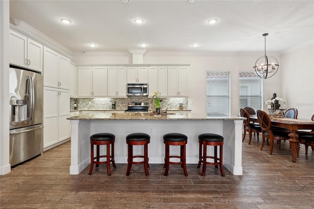 kitchen with light stone countertops, stainless steel appliances, white cabinetry, and a kitchen island with sink