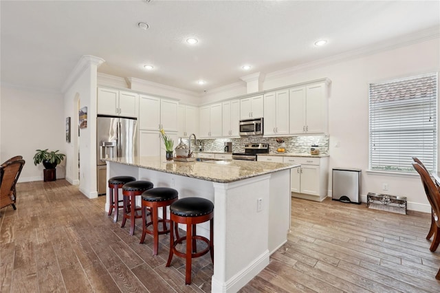 kitchen featuring a center island with sink, stainless steel appliances, white cabinets, light stone counters, and a breakfast bar