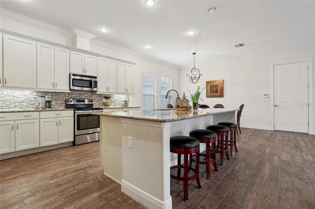 kitchen with pendant lighting, a breakfast bar, a kitchen island with sink, appliances with stainless steel finishes, and white cabinets