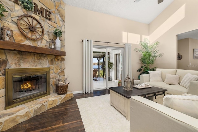 living room featuring ceiling fan, a stone fireplace, and dark hardwood / wood-style floors