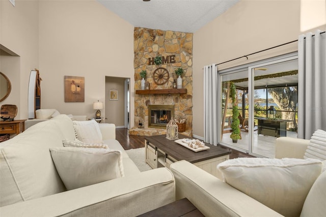 living room with a textured ceiling, a stone fireplace, hardwood / wood-style floors, and high vaulted ceiling