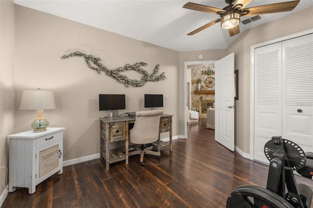 office area with a textured ceiling, ceiling fan, dark hardwood / wood-style floors, and a fireplace