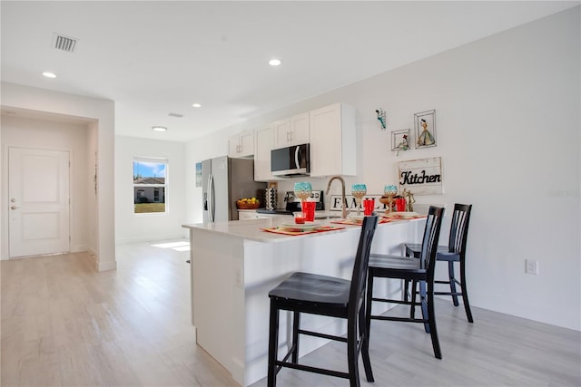 kitchen with white cabinetry, a kitchen breakfast bar, light hardwood / wood-style floors, kitchen peninsula, and stainless steel appliances