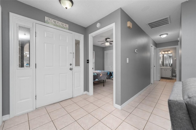 foyer entrance featuring a textured ceiling, ceiling fan, and light tile patterned floors