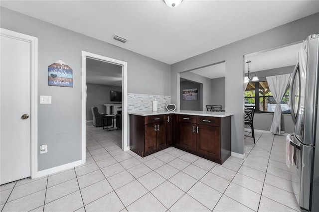 kitchen featuring backsplash, stainless steel refrigerator, dark brown cabinetry, and light tile patterned floors