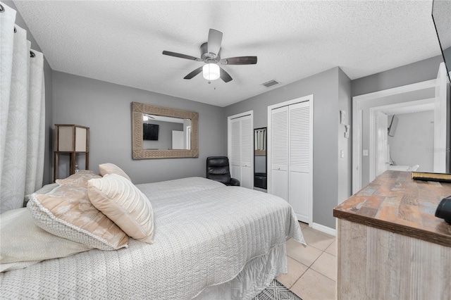 tiled bedroom with a textured ceiling, two closets, and ceiling fan