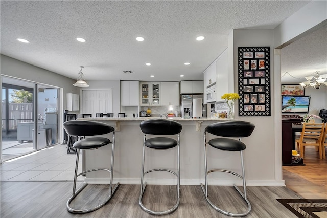 kitchen with white cabinets, stainless steel fridge, light wood-type flooring, a kitchen bar, and kitchen peninsula