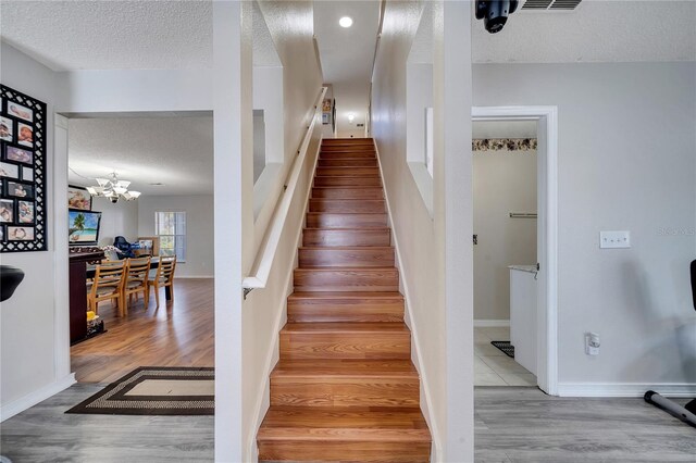 stairs with hardwood / wood-style flooring, a textured ceiling, and an inviting chandelier