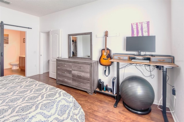 bedroom with a barn door, ensuite bath, and wood-type flooring