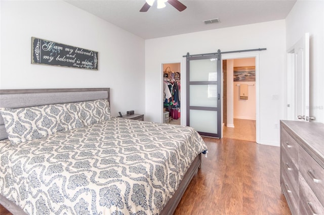 bedroom featuring a spacious closet, ceiling fan, a barn door, dark hardwood / wood-style flooring, and a closet