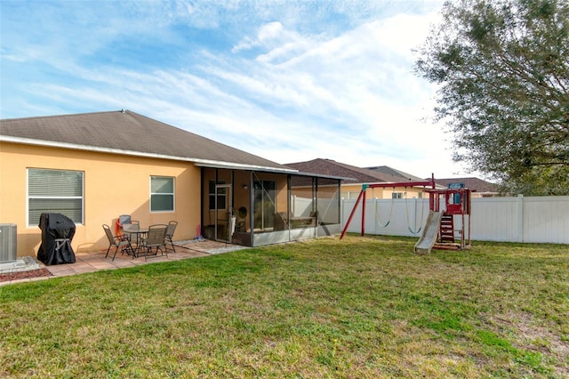 rear view of property with a lawn, a sunroom, a playground, cooling unit, and a patio area