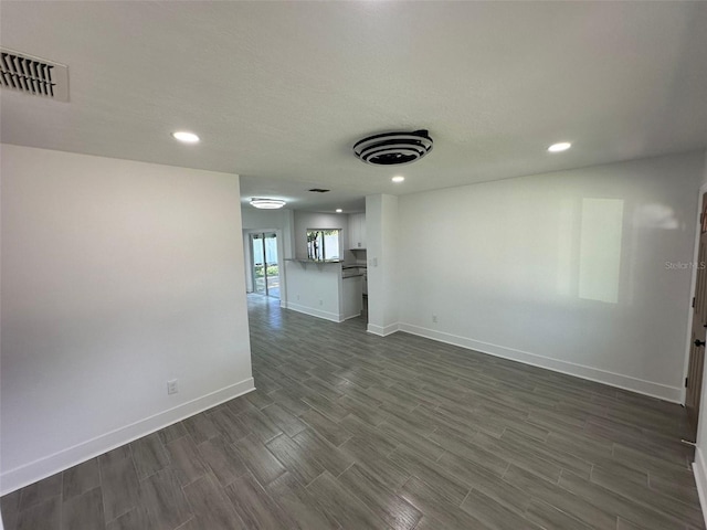 spare room with a textured ceiling, recessed lighting, visible vents, baseboards, and dark wood-style floors