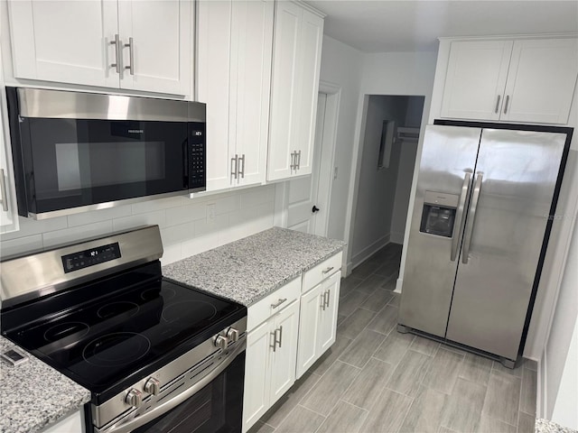 kitchen featuring light stone counters, stainless steel appliances, backsplash, wood tiled floor, and white cabinetry