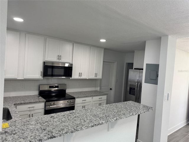 kitchen with stainless steel appliances, white cabinetry, and light stone counters