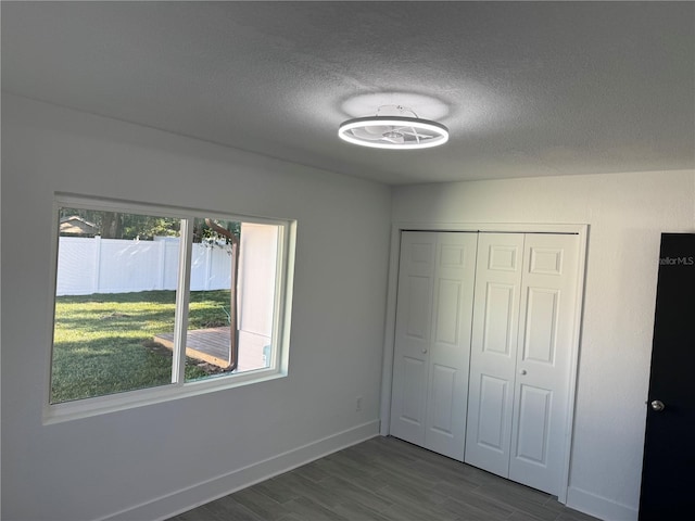 unfurnished bedroom featuring dark wood-style floors, a closet, a textured ceiling, and baseboards