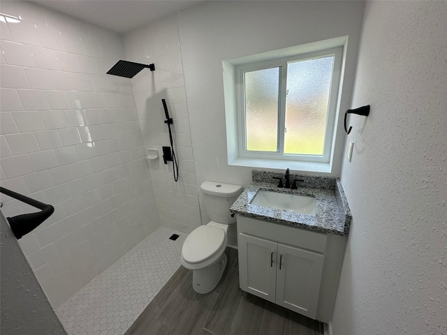 bathroom with a textured wall, a tile shower, vanity, and toilet