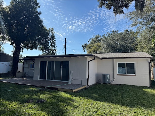 rear view of house with concrete block siding, a patio, a lawn, central AC unit, and fence