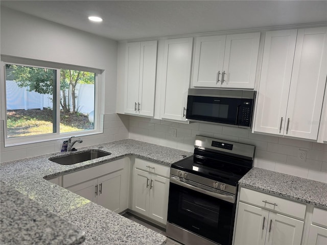 kitchen featuring light stone counters, a sink, white cabinets, appliances with stainless steel finishes, and backsplash