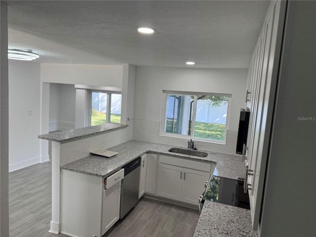 kitchen featuring electric range, stainless steel dishwasher, white cabinets, a sink, and a peninsula