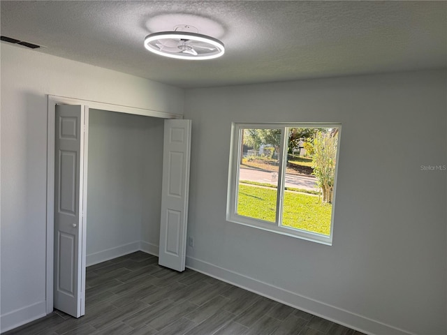 unfurnished bedroom with dark wood-type flooring, visible vents, a textured ceiling, and baseboards