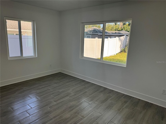 spare room with dark wood-type flooring, plenty of natural light, and baseboards