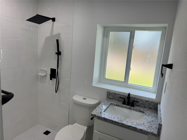 bathroom featuring toilet, tiled shower, and vanity