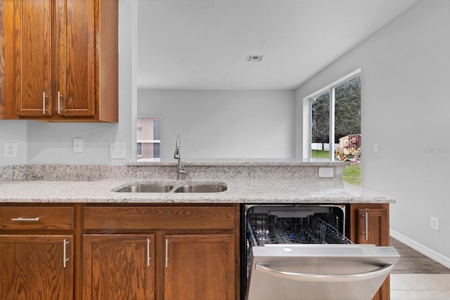 kitchen featuring sink, dishwasher, kitchen peninsula, and light stone countertops