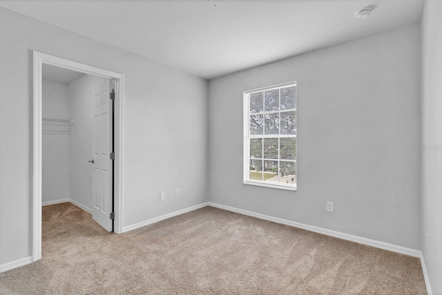 unfurnished bedroom with light colored carpet, a closet, and a spacious closet